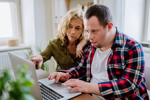 a woman helping a man with a disability on a computer